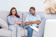 Upset couple sit on a sofa with arms crossed