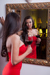 Sensual elegant young woman in red dress looking into mirror