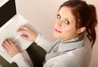 Photo: A young woman with a laptop sitting isolated on grey background A young woman with a laptop sitting isolated on grey background