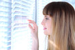 Pretty girl looks out  window through blinds