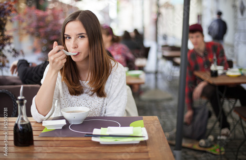 Photo: Young woman eating soup in an restaurant garden Young woman eating soup in an restaurant garden
