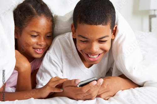Photo: Two Children Using Mobile Phone Under Duvet Two Children Using Mobile Phone Under Duvet