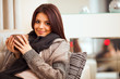 young woman sitting on sofa in cosy cloths with cup of coffee