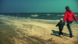 Mother and little boy running on the beach, scaring seagulls