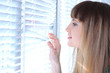 Photo: Pretty girl looks out window through blinds Pretty girl looks out window through blinds