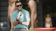 man speaks into a microphone in the background dancing girls
