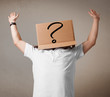 Foto: Young man gesturing with a cardboard box on his head with questi Young man gesturing with a cardboard box on his head with questi