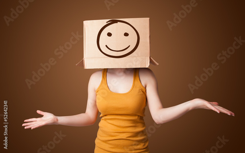 Photo: Young girl gesturing with a cardboard box on her head with smile Young girl gesturing with a cardboard box on her head with smile