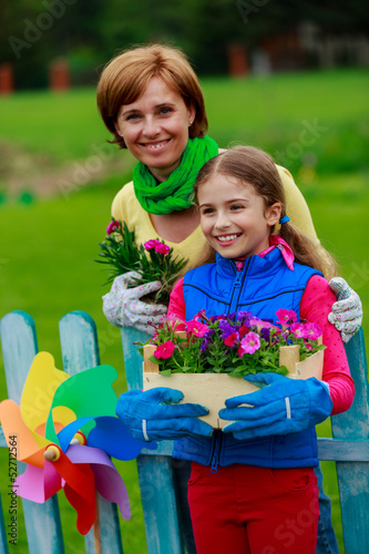Photo: Gardening- lovely girl with mother working in flowers garden Gardening- lovely girl with mother working in flowers garden