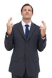Serious businessman with fingers crossed is looking up