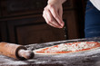 Cook putting oregano on raw pizza