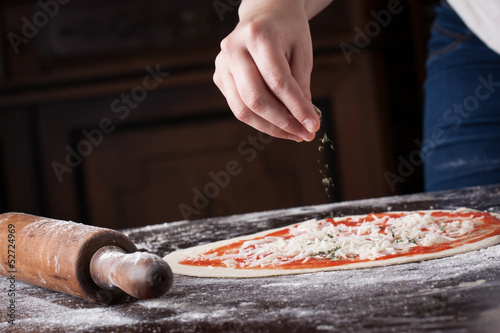 Photo: Cook putting oregano on raw pizza Cook putting oregano on raw pizza
