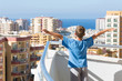 boy stands on balcony and looks into distance holding up hands