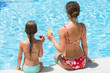 Mother and daughter sitting on edge of pool with drink