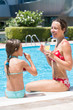 Mother and daughter sitting on edge of pool