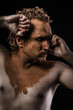 naked man with his face covered in clay, thinking