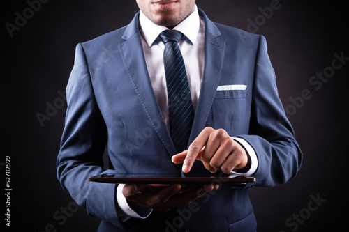 Photo: Businessman working on a digital tablet against black backgroun Businessman working on a digital tablet against black backgroun