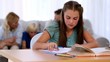 Daughter doing her homework with family on couch behind
