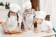Children in clothes cooks in the kitchen preparing a pizza