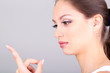 Young woman putting contact lens in her eye on grey background