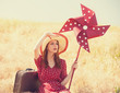 Redhead girl with suitcase and wind turbine sitting at grass