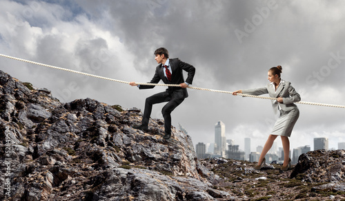 Photo: Two businessmen pulling rope atop of mountain Two businessmen pulling rope atop of mountain