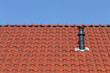 Rotes Dach mit Schornstein vor blauem Himmel