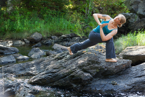 Photo: woman practicing yoga on rocks beside stream woman practicing yoga on rocks beside stream