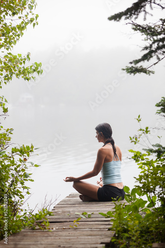 Photo: Woman meditating on dock by lake Woman meditating on dock by lake