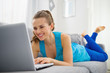 Photo: Happy young woman laying on divan and using laptop Happy young woman laying on divan and using laptop