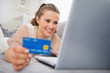 Photo: Happy young woman laying on divan with laptop and credit card Happy young woman laying on divan with laptop and credit card