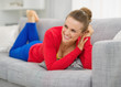Smiling young woman laying on divan in living room