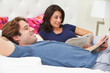 Couple Relaxing In Bed Wearing Pajamas And Reading Newspaper