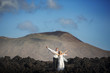 The bride and groom open arms to volcanic landscape background.