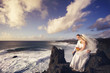 The bride and groom are sitting and looking at the ocean.