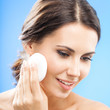 Young woman cleaning skin by cotton pad, over blue