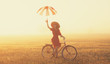 Girl with umbrella on a bike in the countryside in sunrise time