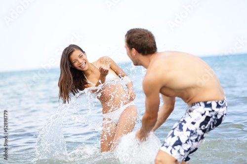 Photo: Beach summer fun couple playful splashing water Beach summer fun couple playful splashing water