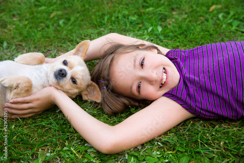 Photo: children girl playing with chihuahua dog lying on lawn children girl playing with chihuahua dog lying on lawn