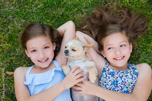 Photo: twin sisters playing with chihuahua dog lying on lawn twin sisters playing with chihuahua dog lying on lawn