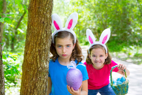 Photo: Easter girls playing on forest with bunny teeth gesture Easter girls playing on forest with bunny teeth gesture
