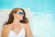 Photo: Young woman relaxing on chaise-longue at poolside Young woman relaxing on chaise-longue at poolside