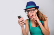 Foto: Funny girl with hat and eyeglasses showing smartphone Funny girl with hat and eyeglasses showing smartphone