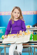 Girl With Book Sitting On Desk In Classroom
