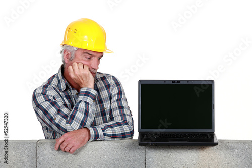 Photo: Confused middle-aged builder looking at laptop Confused middle-aged builder looking at laptop