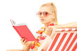 Attractive blond female sitting on a sun lounger and reading a b