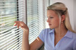 Blond office worker peering through window blinds