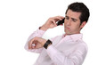 A businessman over the phone looking at his watch.