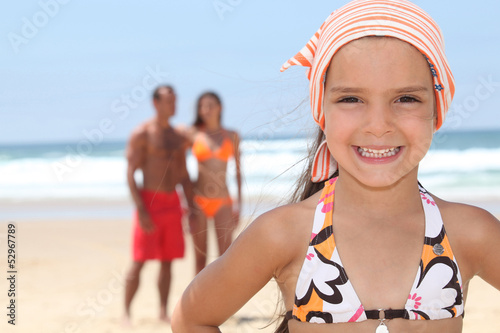 Photo: Young girl at the beach with her parents Young girl at the beach with her parents