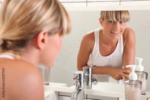 Photo: Young woman looking in the bathroom mirror Young woman looking in the bathroom mirror